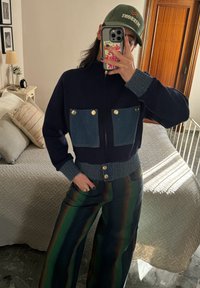 Ναυτικό φούτερ με φερμουάρ και τσέπες από τζιν στο στήθος, με ρα�μμένες μανσέτες και στρίφωμα. Πανάκριβες παντελόνες σε πράσινες και καφέ ρίγες με φαρδιά ποδιά. Πράσινο καπέλο με λογότυπο.