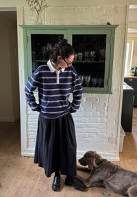 Mörkblå och vitrandig långärmad polo med vit krage, matchad med en svart kjol och svarta skor; en brun hund är i närheten.