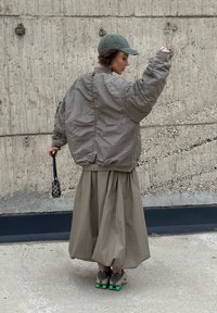 Oversized grey bomber jacket, beige voluminous skirt, green cap, black patterned bag, and beige-grey trainers with green accents.