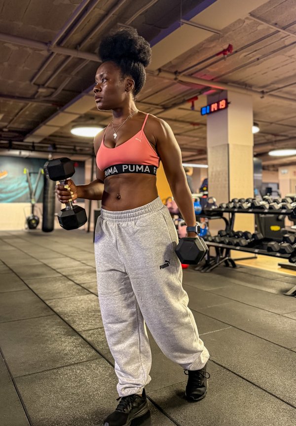 Kvinne på treningssenter iført sports-bh og joggebukse holder manualer, forbereder seg på styrketrening.