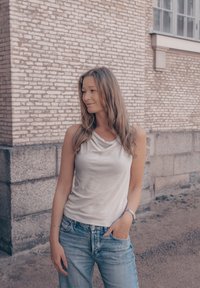 Top senza maniche beige chiaro con scollo drappeggiato abbinato a jeans in denim azzurro. Tessuto morbido, vestibilità rilassata.
