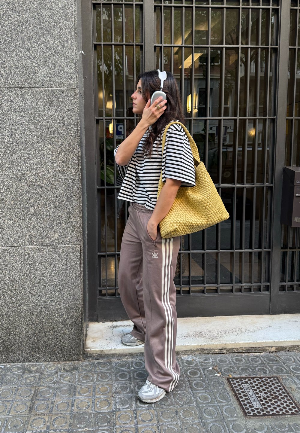 Svītrots īss tops melnbaltā krāsā, brūnas sporta bikses ar baltām svītrām, dzeltena austā somiņa un pelēkas sporta kurpes. Uz ausīm austiņas.