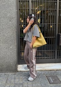 Svītrots īss tops melnbaltā krāsā, brūnas sporta bikses ar baltām svītrām, dzeltena austā somiņa un pelēkas sporta kurpes. Uz ausīm austiņas.