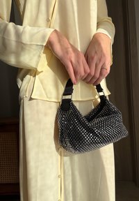 Mustast ja hõbedasest helmestega käekott, millel on kõver kujundus, tekstuuriga pind, lühikesed mustad sangad ja nähtavad metallikdetailid.