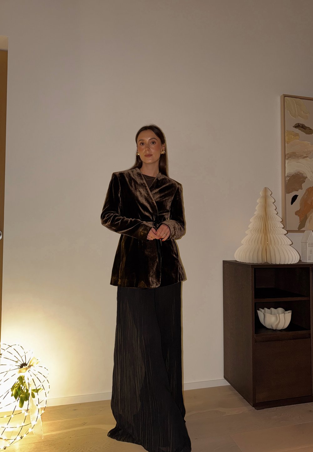 Velvet brown blazer with a shawl collar, paired with a black pleated skirt. Background features a lighted sphere and decorative tree.