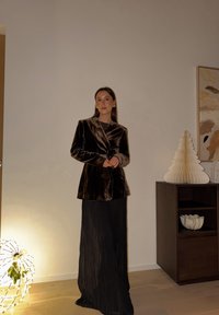Velvet brown blazer with a shawl collar, paired with a black pleated skirt. Background features a lighted sphere and decorative tree.