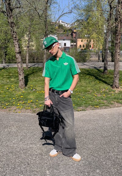 Polo de rayas verdes con acentos blancos; jeans de pierna ancha gris oscuro; bolso negro; zapatillas blancas con suelas marrones; al aire libre con hierba y árboles.