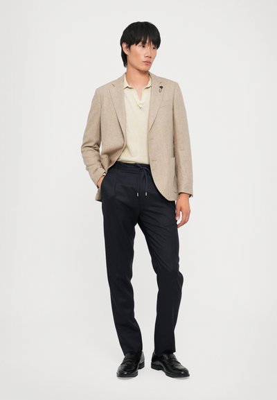 Blazer de mezcla de lino beige, camiseta polo amarilla clara con rayas sutiles, pantalones navy con cordón y mocasines negros. Diseño simple y elegante.