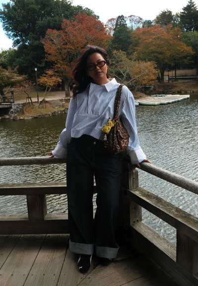 Camisa a rayas con cuello blanco recortada, jeans oscuros de pierna ancha y zapatos negros. Los accesorios incluyen un bolso de estampado de leopardo y juguetes de peluche.