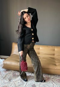 Cardigan preto em mistura de lã com três botões dourados e um detalhe em forma de estrela, combinado com calças flare em padrão de cobra verde e uma bolsa estruturada vermelha.