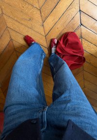 Άτομο με μπλε τζιν και κόκκινα παπούτσια στέκεται σε ξύλινο δάπεδο δίπλα σε μια κόκκινη τσάντα που βρίσκεται στο πάτωμα.