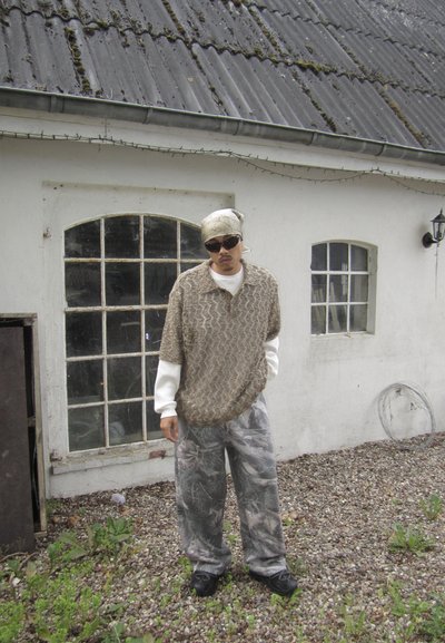 Conjunto casual que incluye una camisa corta de manga larga marrón texturizada, una camisa larga blanca debajo, pantalones de camuflaje y zapatos negros.