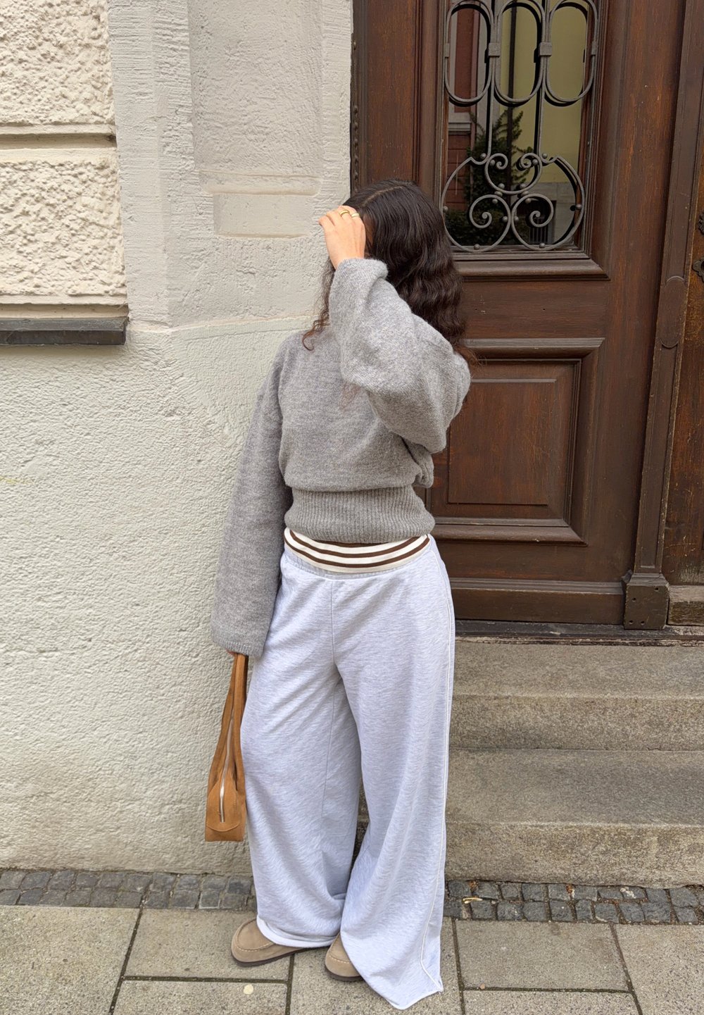 Lysegrå oversized sweater med løse ærmer kombineret med grå, vidtbens sweatpants. Brun og hvid stribet linning. Brun håndtaske.