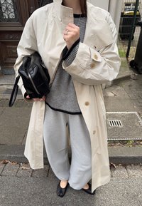 Beež kerge trench coat, mustriba särk, hallid dressipüksid ja mustad korterid. Hoides väikest musta käekotti.