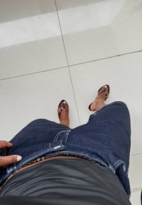 Shorts in denim blu scuro con dettagli scoloriti, abbinati a sandali neri con design a striscia sottile. Top nero liscio visibile.