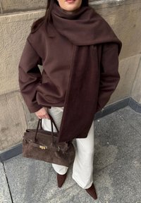 Rjavo večje plašč z zavesljenim šalcem, kombiniran z lahkimi hlačami in temno rjavo torbico iz semiša. Izgled dopolnjujejo rjavi špičasti čevlji.