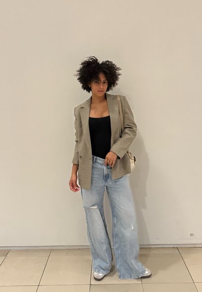 Blazer a cuadros grises sobre una blusa negra, combinado con jeans de pierna ancha de mezclilla clara y desgastada, y zapatos plateados. Un look casual pero estructurado.