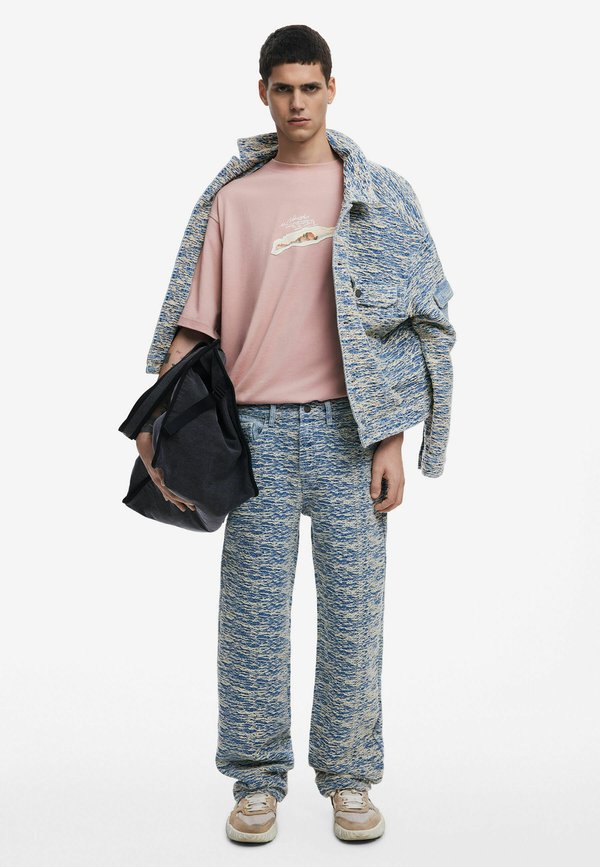 Blau-weiße strukturierte Strickjacke und -hose, kombiniert mit einem rosa T-Shirt mit kurzen Ärmeln und grafischem Print. Schwarze Tragetasche in der Hand.