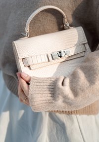 Sac à main structuré en matériau texturé beige clair avec une forme rectangulaire, doté d'une fermeture à fermoir et d'une anse courte.