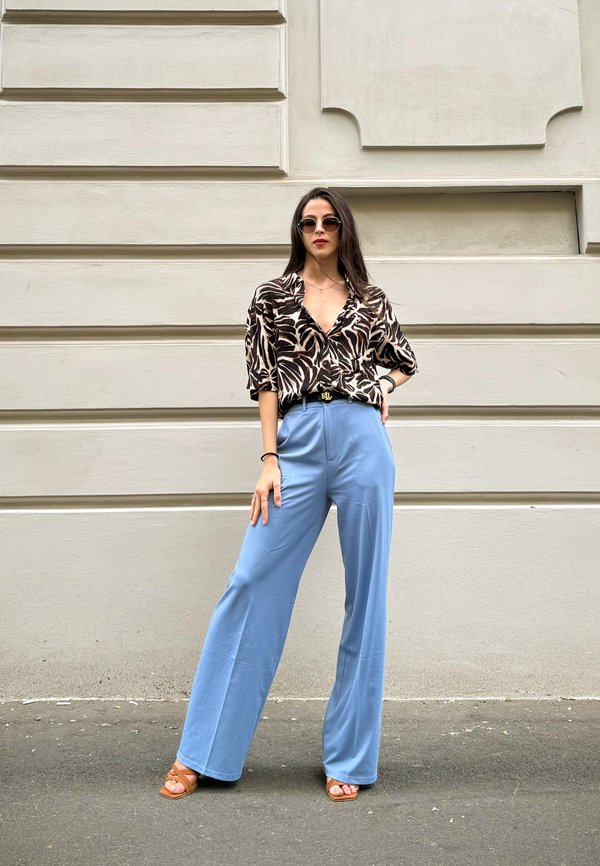 Pantalones anchos y fluidos en azul, combinados con una camisa de manga corta con estampado de hojas en blanco y negro. Los accesorios incluyen gafas de sol y un cinturón negro.