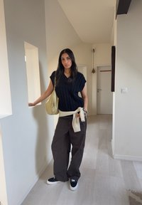 Haut noir en maille torsadée, ceinture à la taille beige clair, pantalon large marron, baskets noires avec semelles blanches, et sac à bandoulière beige clair.