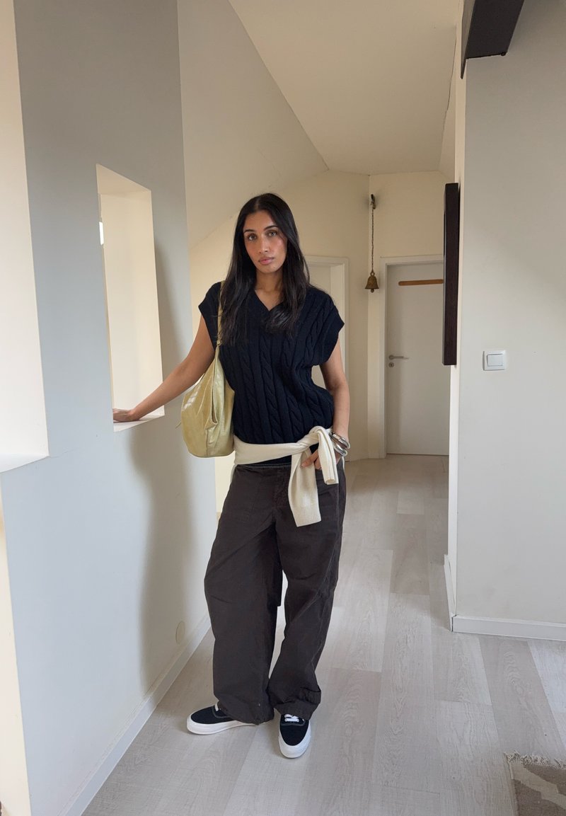 Haut noir en maille torsadée, ceinture à la taille beige clair, pantalon large marron, baskets noires avec semelles blanches, et sac à bandoulière beige clair.