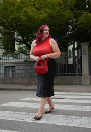 Top rojo ajustado combinado con una falda midi negra, acentuado por un bolso texturizado rojo y zapatos de tacón con estampado de leopardo. Caminando por un paso de peatones.