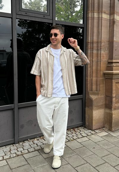 Camisa de manga corta a rayas en beige y crema, camiseta blanca, pantalones blancos holgados y zapatos cerrados en colores claros.