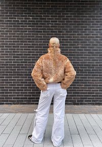 Casaco de pele sintética castanho com manchas, com gola alta, combinado com calças cargo brancas com bolsos e cordões, visto de costas.