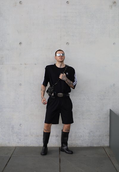 Conjunto atlético negro con una camiseta holgada de manga corta y pantalones cortos, complementado con botas negras hasta la rodilla y gafas de sol espejadas.