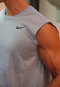 Light purple sleeveless Nike sports top, featuring a black logo on the chest, smooth texture, and fitted design highlighting a muscular shape.