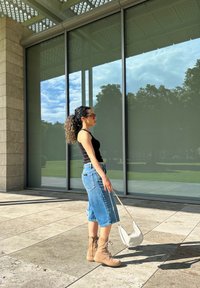 Uformell antrekk med en svart tanktop, lyseblå vide denimshorts og beige snørefottøy, komplettert med en liten hvit veske.
