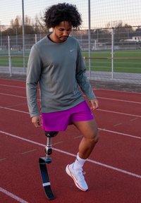 Idrettsutøver med kort krøllete hår, iført en grå genser med lange ermer og lilla shorts, som bruker et svart protetisk ben på en rød løpebane.
