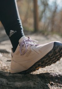 Scarpa da ginnastica rosa chiaro con lacci viola, suola in gomma testurizzata e punta rinforzata, indossata con un calzino nero con logo.