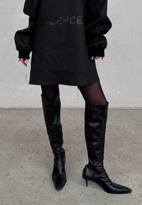 Μαύρες δερμάτινες μπότες μέχρι το γόνατο, με στιλέτο τελείωμα και λεπτό τακούνι. Ο σχεδιασμός έχει ματ υφή και ελάχιστες μεταλλικές λεπτομέρειες.