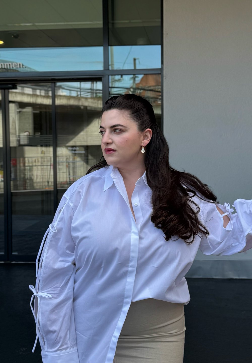 Camisa blanca de botones con mangas abiertas atadas con lazos, combinada con una falda beige. Tejido suave, ajuste holgado y cuello puntiagudo.