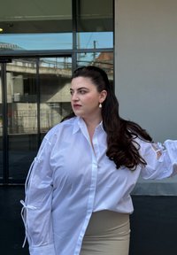 Camisa blanca de botones con mangas abiertas atadas con lazos, combinada con una falda beige. Tejido suave, ajuste holgado y cuello puntiagudo.