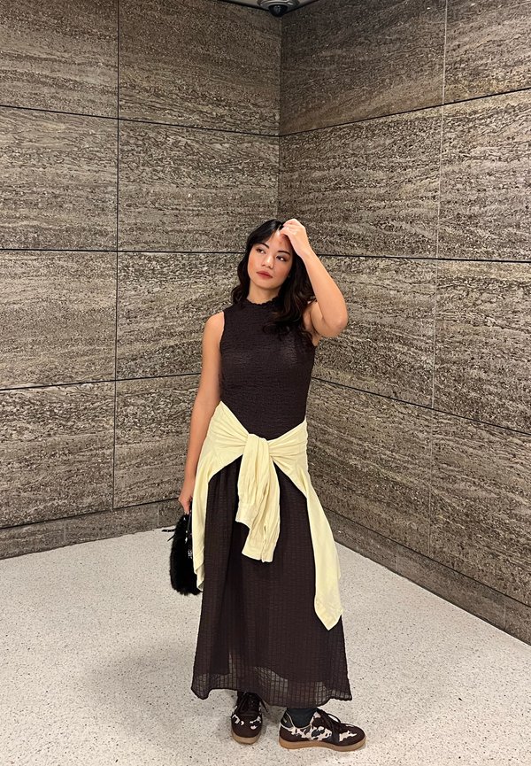 Vestido maxi com parte superior castanho chocolate texturizada e saia fluida; sweater creme atado à cintura; bolsa preta felpuda; sapatos estampados.