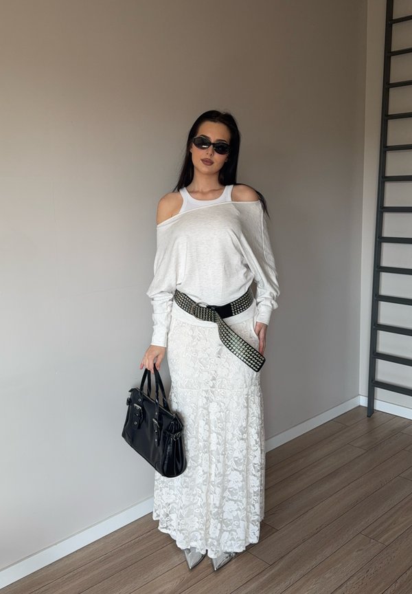 Hvid off-shoulder top, lang hvid blonde nederdel, sort naglefæstet bælte, sort håndtaske og sølv spidse støvler, med solbriller. Minimalistisk baggrund.