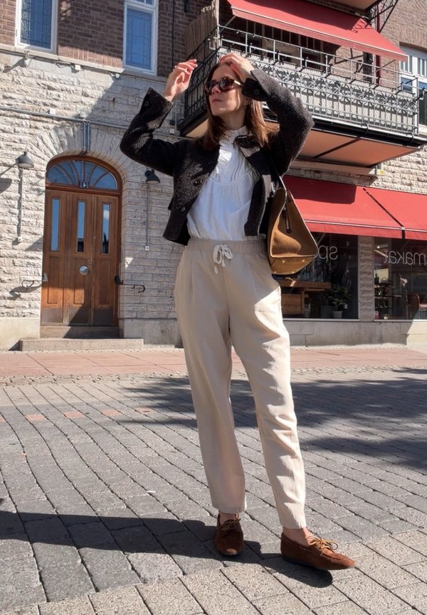 Woman adjusting sunglasses standing on a cobblestone street near a stone building with red awnings and wooden door.