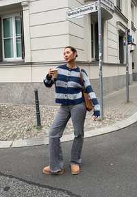 Sinine ja hall triibuline kootud kardigan nööpidega, hallid teksad ja beežid pahkluu saapad. Hoides kohvitassi, seistes tänavanurgal.