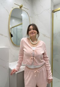Completo da casa rosa chiaro a coste con cardigan corto e pantaloncini abbinati. Presenta lacci all'altezza del collo e orli arricciati. Sfondo marmo.