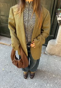 Blazer v vzorju houndstooth v olivno zeleni barvi, črna majica na zadrgo, modri ohlapni kavbojke, rjava usnjena torba in temni čevlji z zlatimi verižnimi detajli.