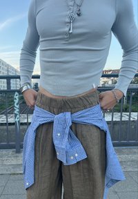 Jasno szary long-sleeve henley, brązowe lniane spodnie z elastycznym pasem oraz niebieska koszula w kratę związana na talii. Akcenty w postaci srebrnej biżuterii.