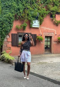 Μαύρο τοπ με έναν ώμο και λευκές πουά, λευκές σόρτσες και μαύρη τσάντα. Λευκά σανδάλια με τετράγωνη φτέρνα και γυαλία ηλίου ολοκληρώνουν την εμφάνιση.