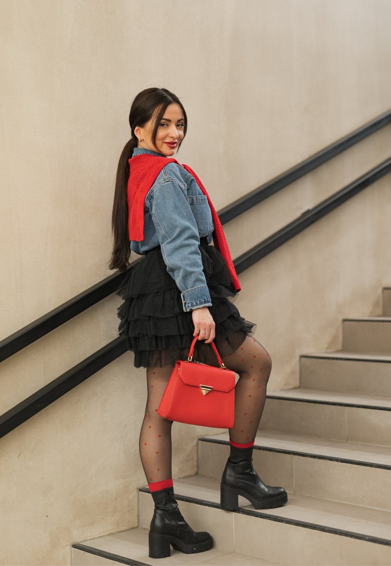 Young woman ascending stairs wearing a denim jacket, black tiered skirt, patterned stockings, red scarf, and carrying a red handbag.