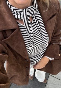 Brown suede coat with large lapels, black and white striped top, white flared trousers, and brown shoes. A knotted striped scarf around the neck.
