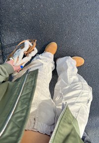 Botas de tobillo marrones, pantalones cargo beige con puños elásticos y una chaqueta acolchada verde oliva. Se lleva un bolso de pelo blanco en la mano izquierda.