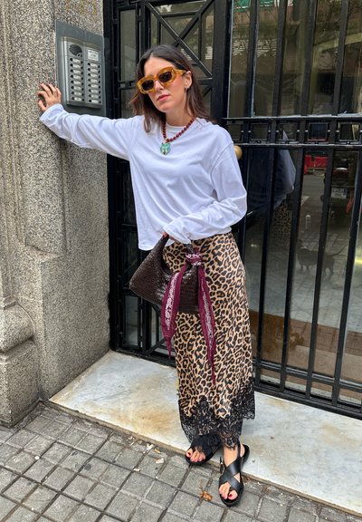 Top blanco de manga larga, falda de leopardo con encaje, gafas de sol amarillas extragrandes, bolso de mimbre marrón con una bufanda en granate, sandalias negras.