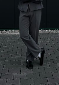 Γκρι παντελόνι με φαρδιά εφαρμογή, συνδυασμένο με γυαλιστερά μαύρα παπούτσια. Το ύφασμα φαίνεται λείο και το παντελόνι έχει χαλαρή εφαρμογή και ρίγα.